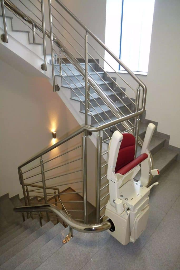 Stairway with a Handicare Freecurved stairlift and metal rail in a modern well-lit interior.