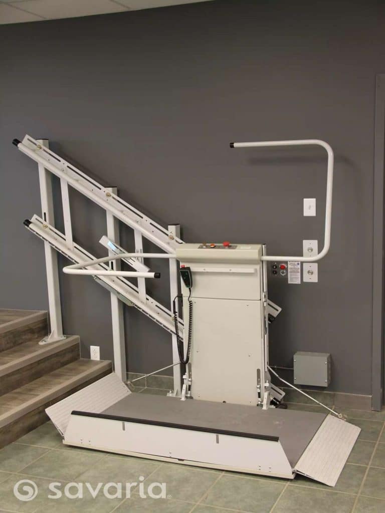 Savaria Delta incline platform lift installed next to a short staircase featuring a rail system, safety handle and control box.