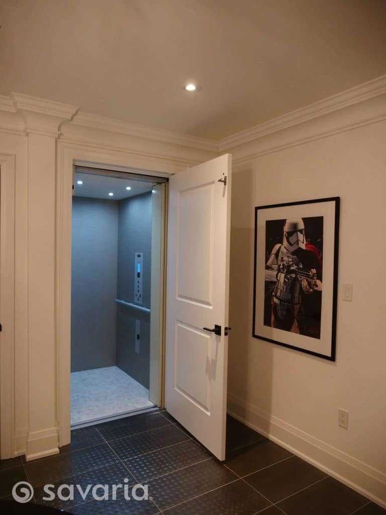 Savaria Infinity Open Residential Elevator with light blue gray interior and framed poster on adjacent wall.