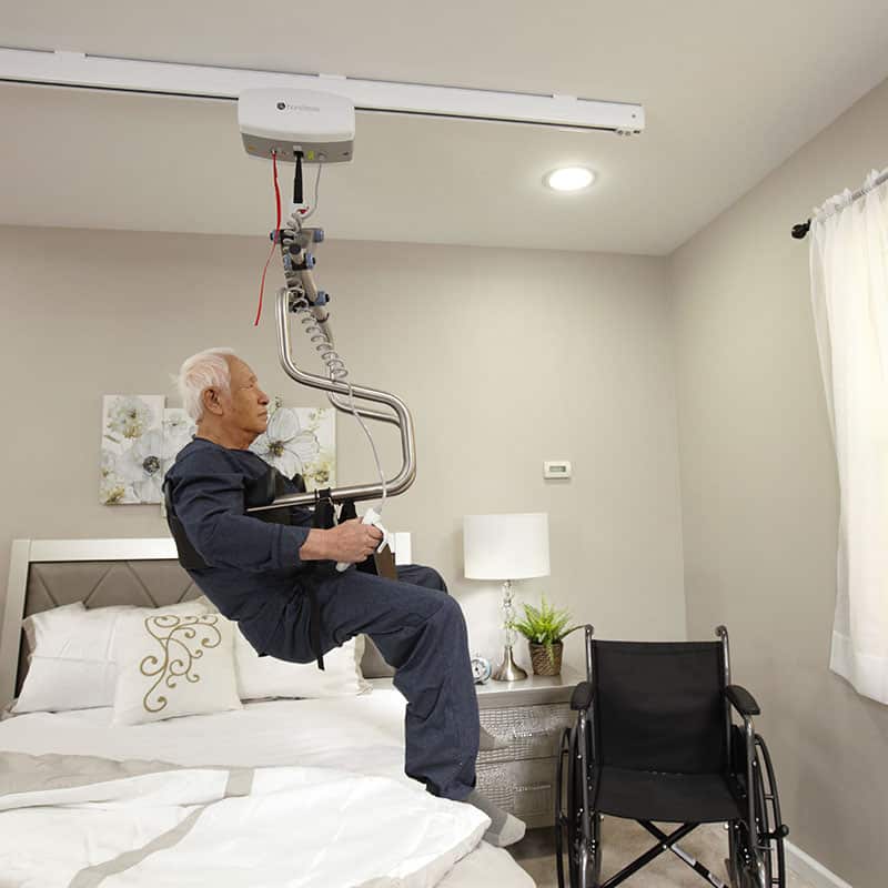 A person is being lifted by Handicare C-450 ceiling mounted transfer lift in a bedroom.