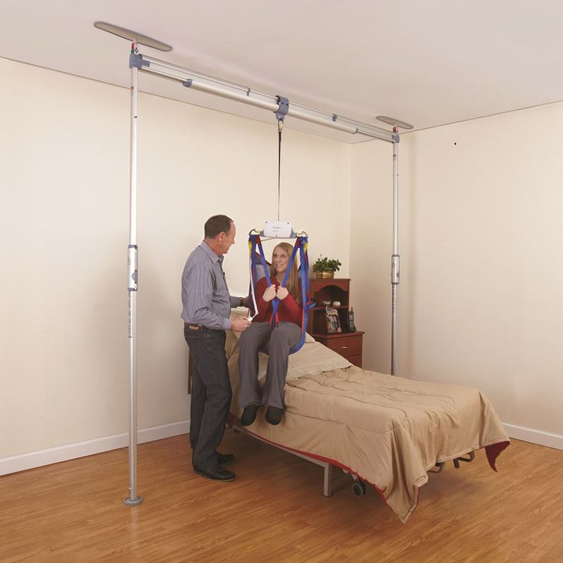 Pressure-fit ceiling lift system installed in a home and a man explaining its practical application to a woman patient.