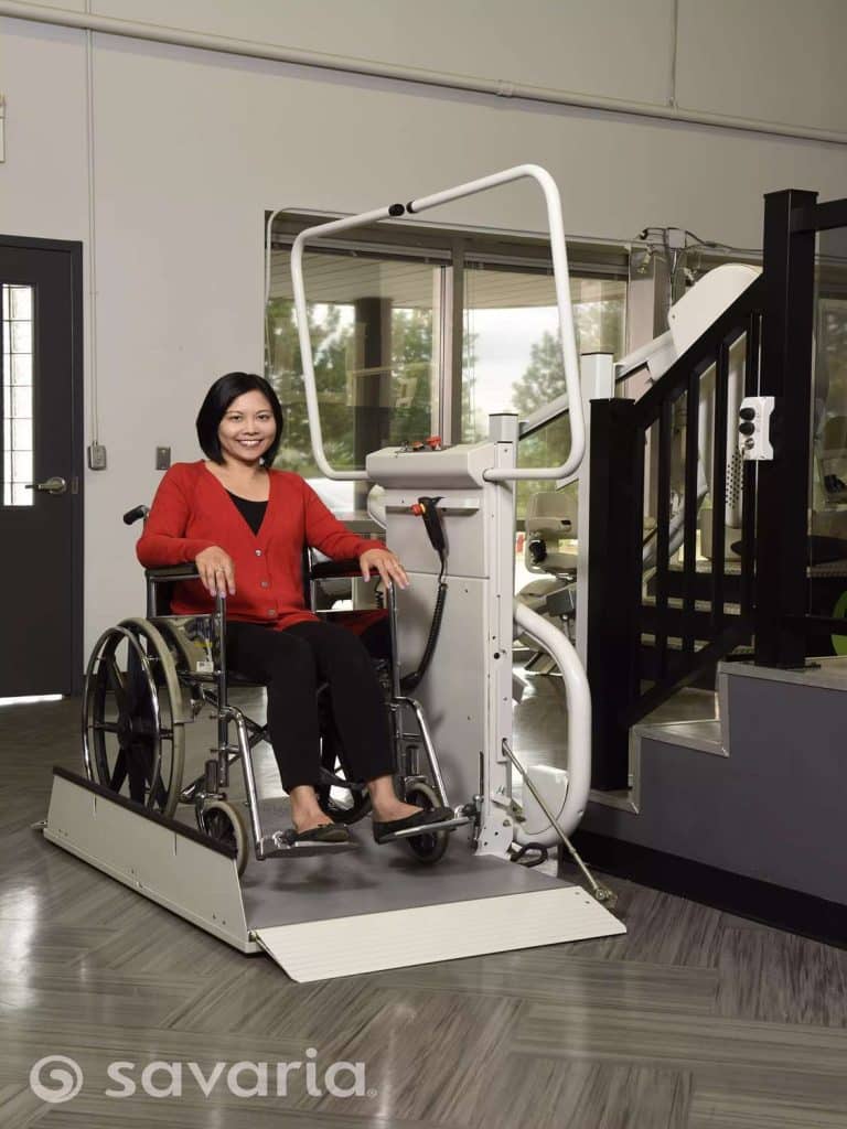 Woman using a Savaria Omega Inclined Platform Lift wheelchair model beside a staircase indoors.