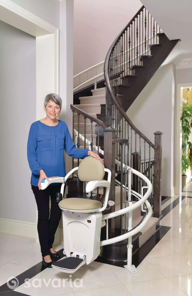 Woman standing next to a Savaria Stairfriend 23 Stairlift on a spiral staircase in a modern home.