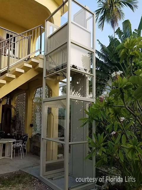 Outdoor Residential Savaria V-1504 Vertical Platform Lift beside a yellow building with an external staircase.