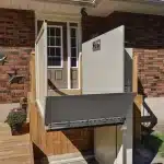 Savaria Multi lift Outdoor Residential Platform lift next to a brick house with a wooden deck.