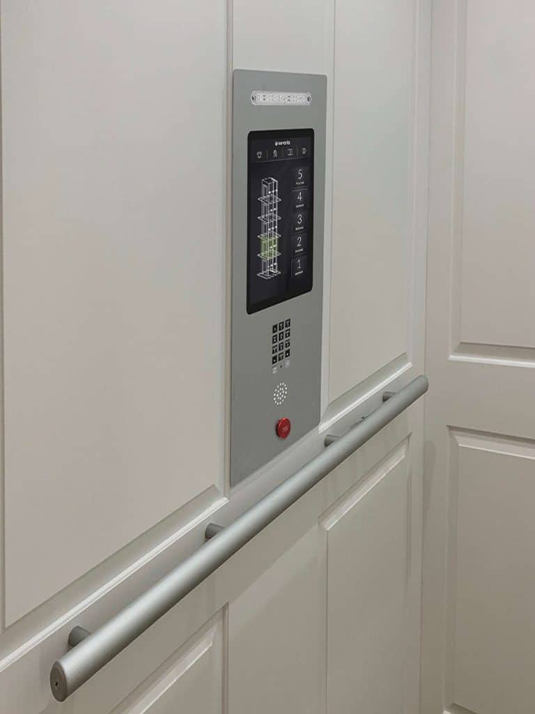 Savaria Zenith Home Elevator Interior With Digital Touchscreen Control Panel and Silver Handrail On White Wall.