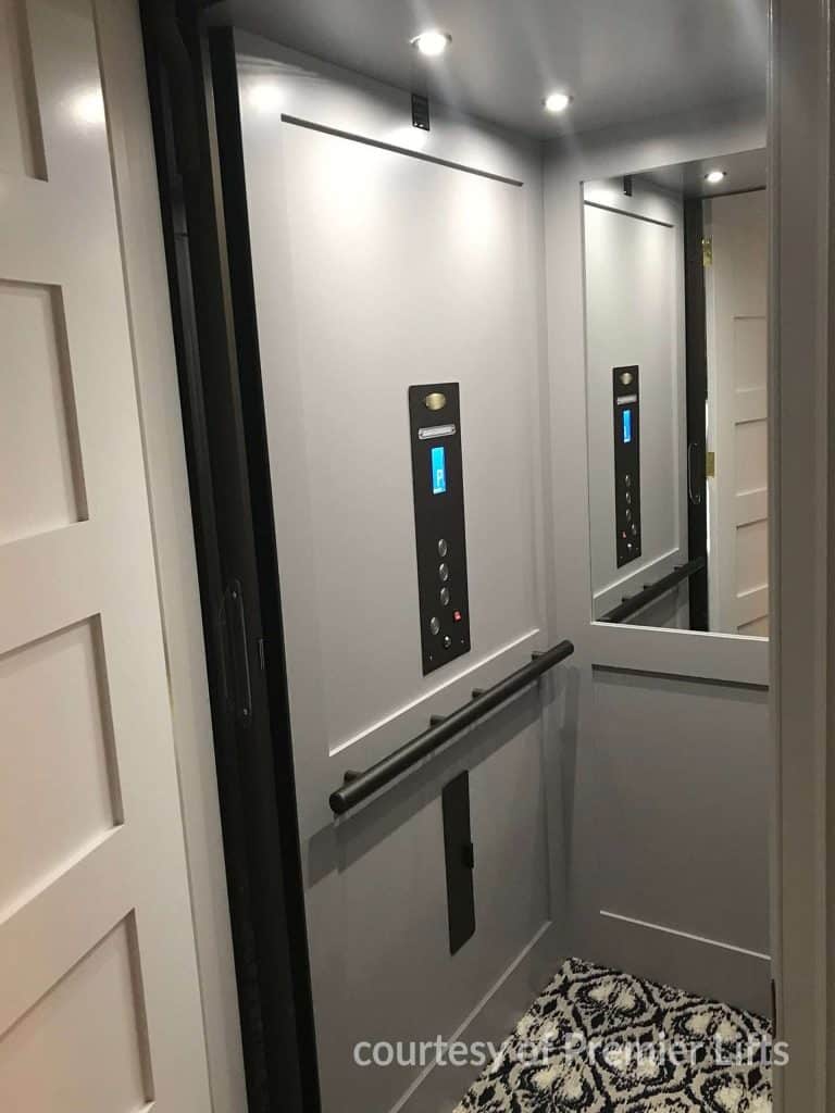 Interior of Small Modern Savaria Eclipse Home Elevator With Gray Walls a Control Panel with recessed lighting and Patterned Rug.