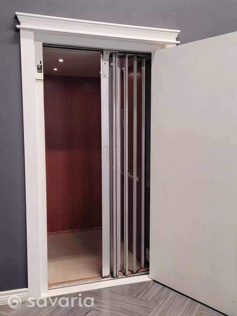 Savaria Eclipse Open Residential Elevator with Folding Metal Gate and Wood Paneled Interior.