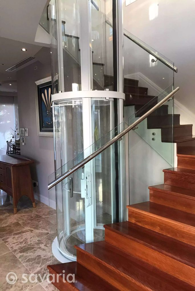 Savaria Vuelift Mini Glass elevator installed beside a wooden staircase in a modern interior.