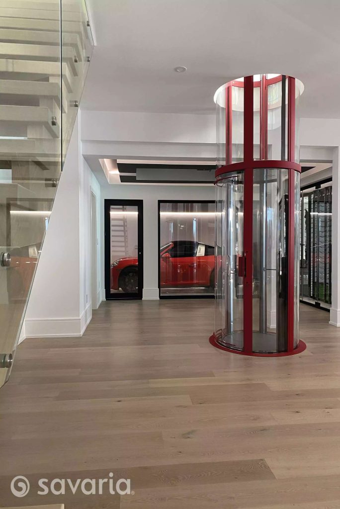 Savaria Vuelift Mini modern interior with a glass elevator, a staircase with glass railings, and a red car visible through glass doors.