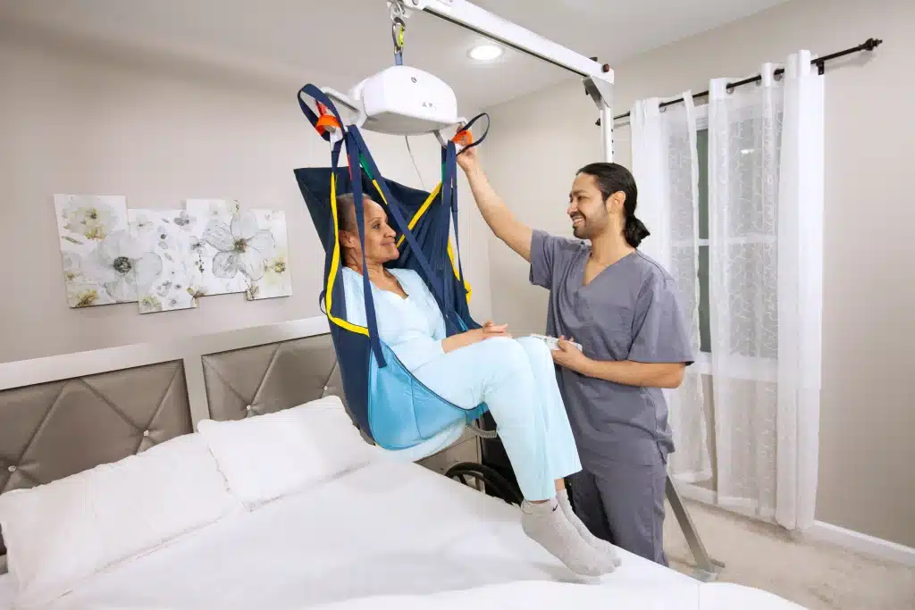 Patient in a lift sling with caregiver, showcasing safe mobility support from a ceiling lift in a home care setting