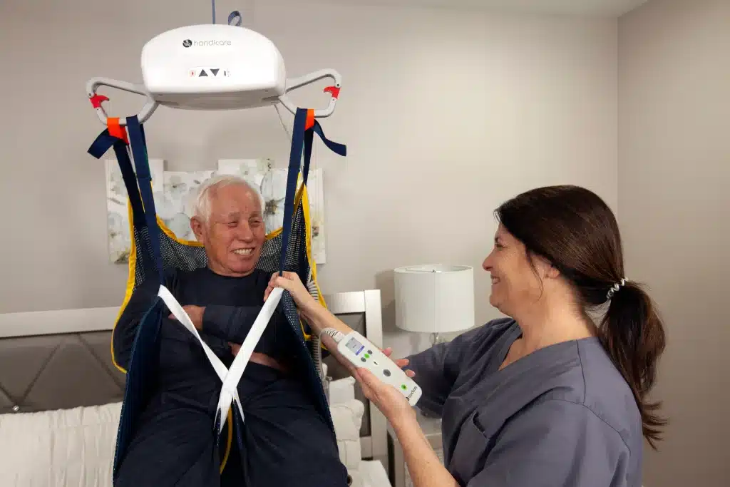 Elderly man in Handicare AP Series Portable Ceiling Lift smiling at a woman operating the lift.