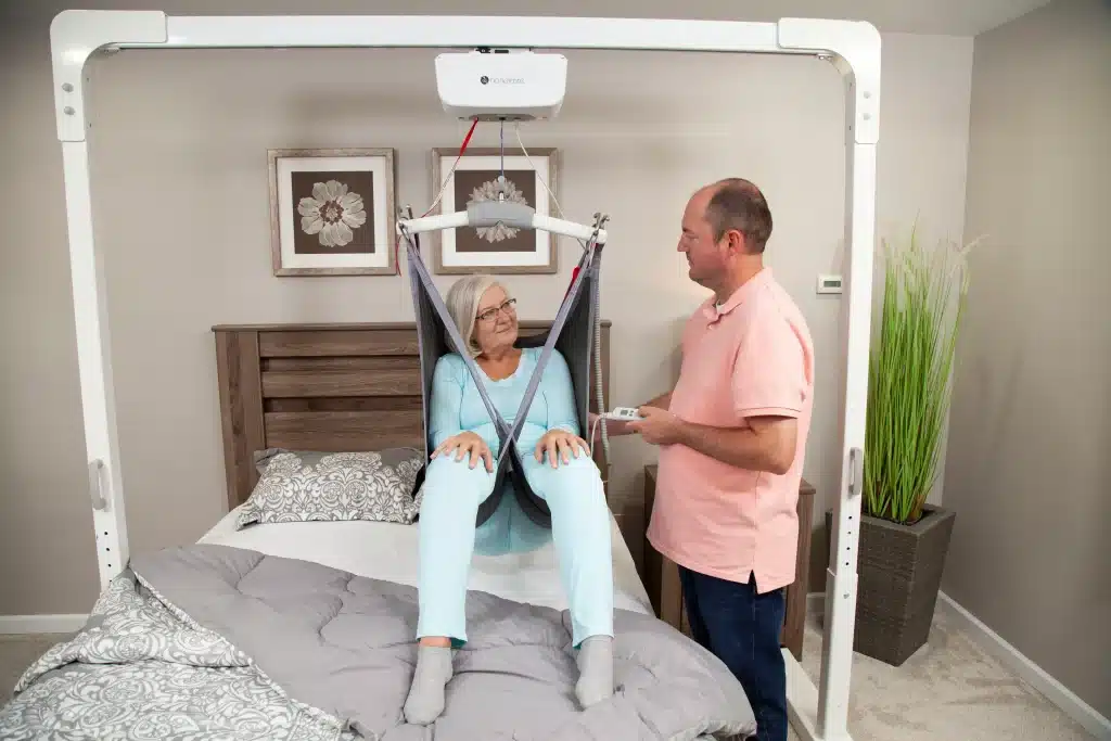 Handicare ceiling lift with a man in a pink shirt adjusting it for a patient showcasing its ergonomic design another view 3.