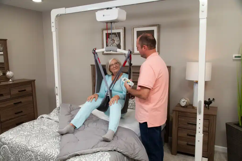 Handicare ceiling lift with a man in a pink shirt adjusting it for a patient showcasing its ergonomic design another view 2.