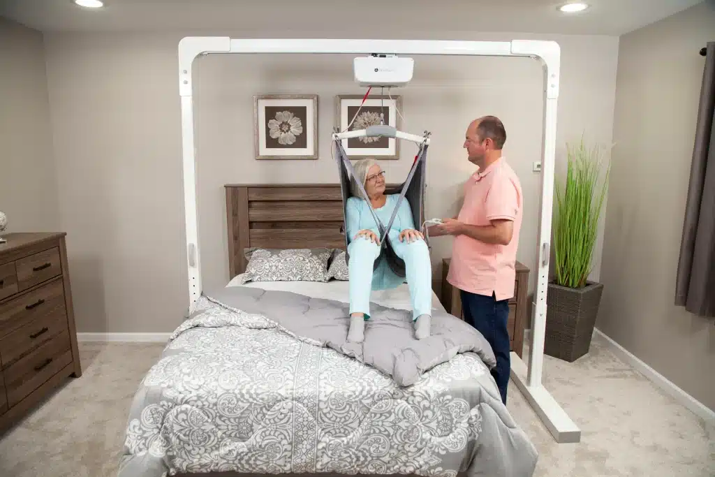 Handicare ceiling lift with a man in a pink shirt adjusting it for a patient showcasing its ergonomic design.