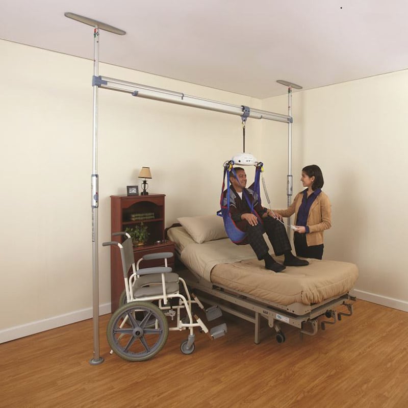 Pressure-fit ceiling lift system installed in a home with a nurse adjusting it for an elderly patient highlighting the track and support structure.