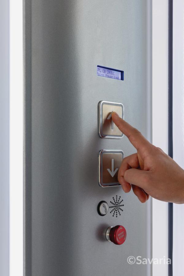 A hand pressing a button on Savaria Luma home elevator control panel with a digital display and various controls.