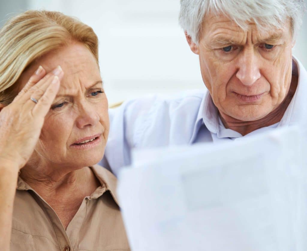 Elderly couple looking concerned while examining a document.
