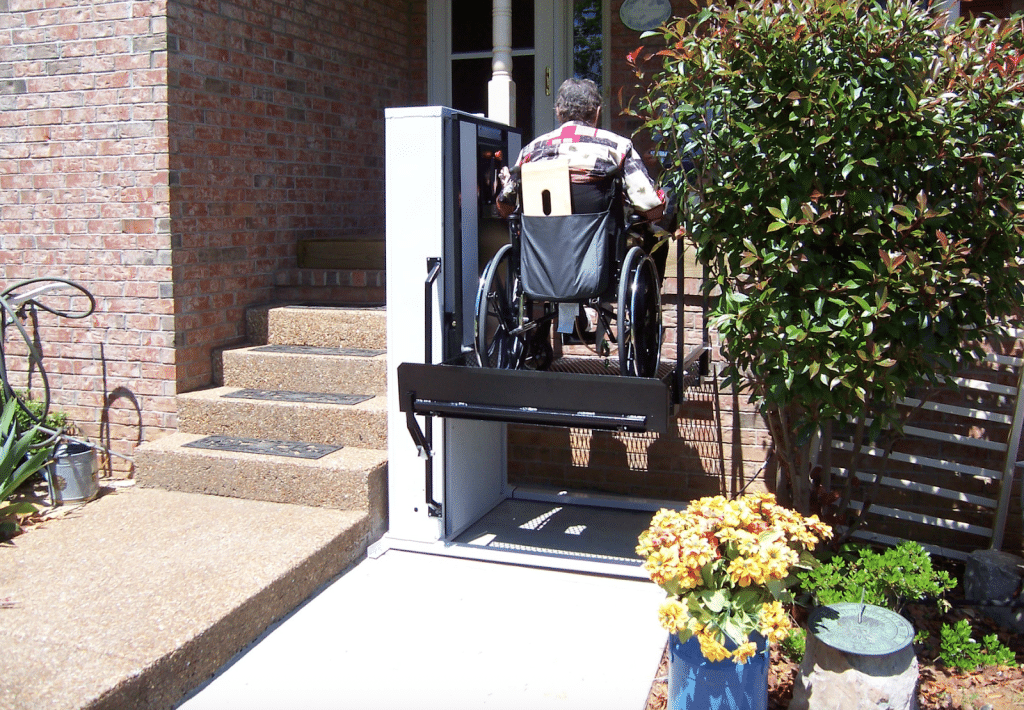 A wheelchair lift in use at the entrance of a brick house.