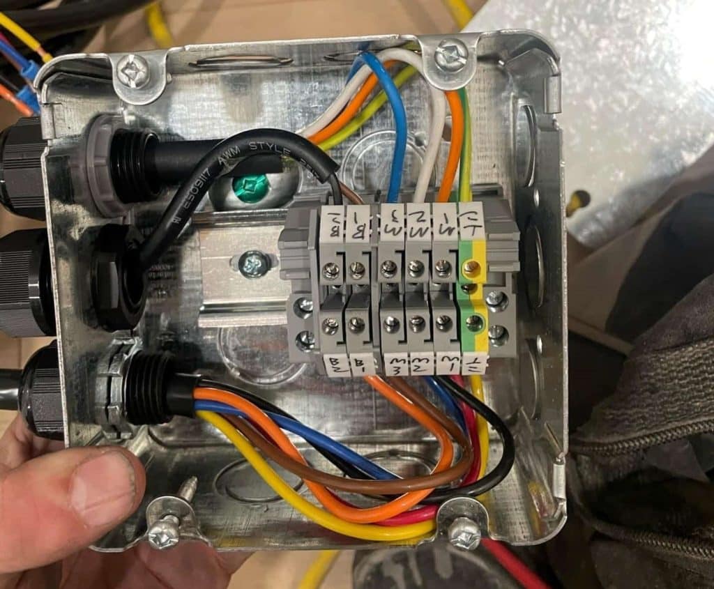 Interior of a metal electrical junction box with multicolored wires and terminal block.