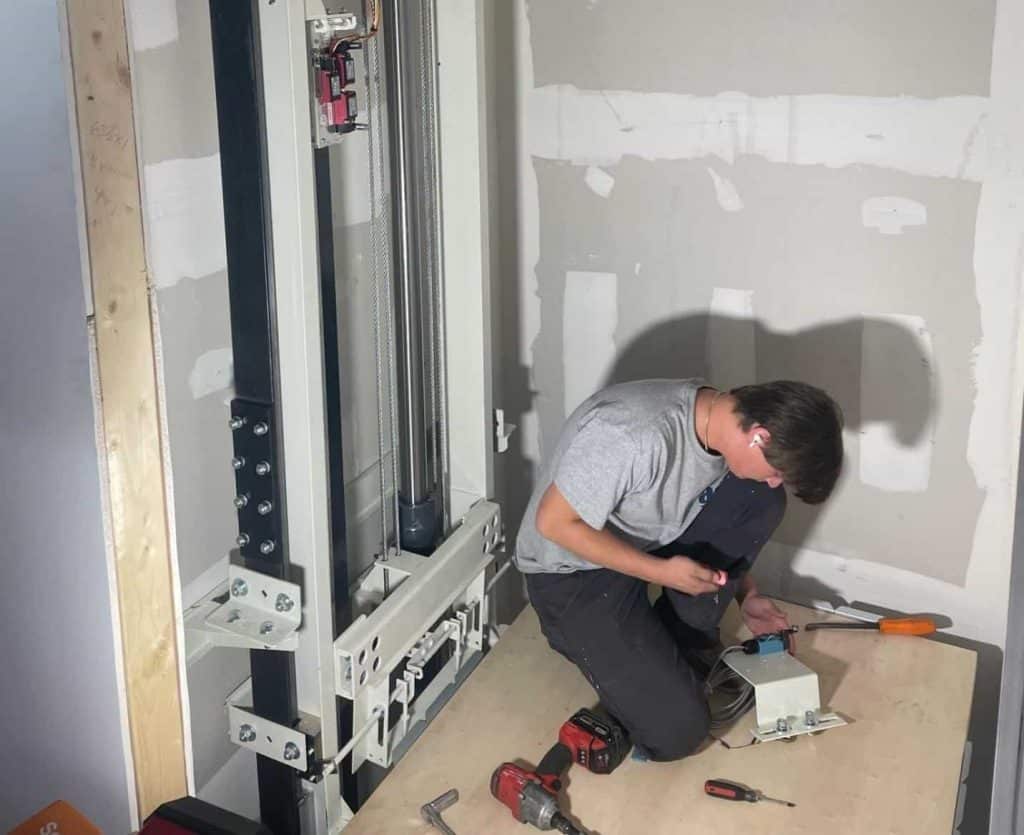 A person working on a vertical rail system inside an unfinished wall section.