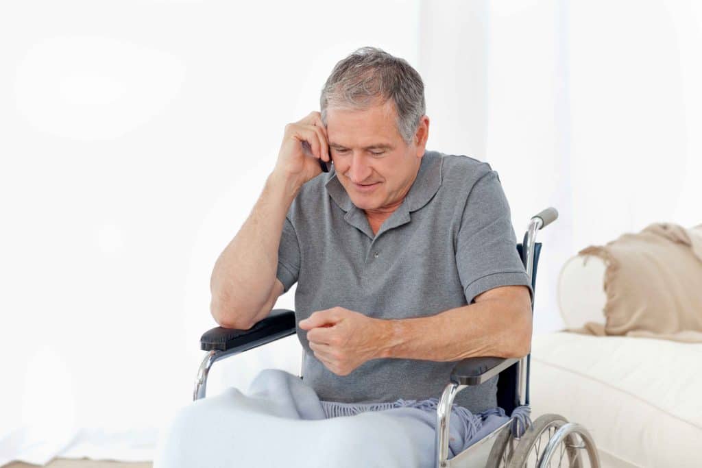 Older man in a wheelchair talking on a phone indoors.