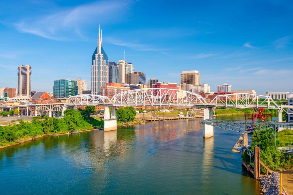 Cityscape with a bridge over a river and modern buildings in the background against a blue sky.