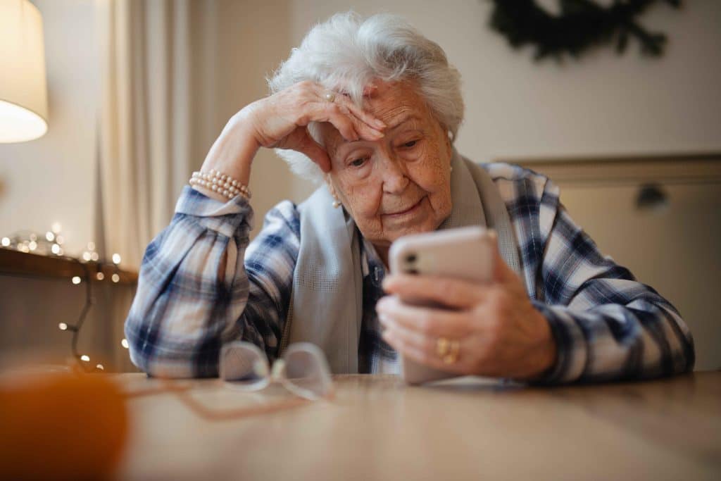 Elderly woman holding a smartphone at a table with glasses.
